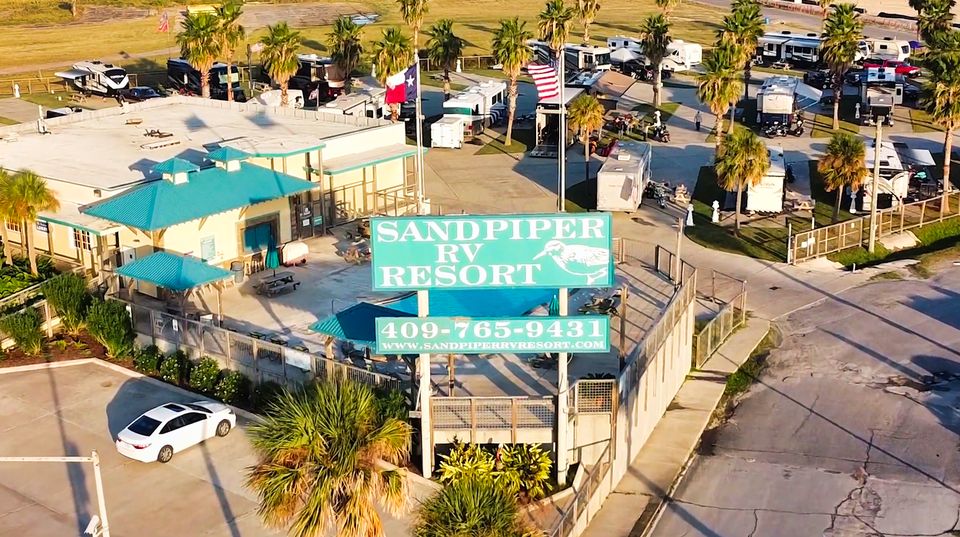 Aerial view of Sandpiper RV Resort at golden hour, the clubhouse sign and palm rows with RVs parked on concrete pads