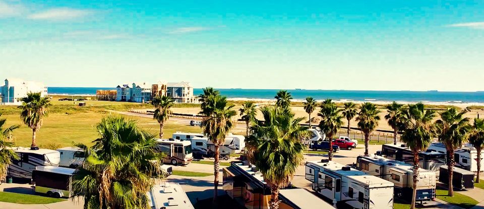 RVs parked under palms with the beach and open Gulf beyond the Seawall