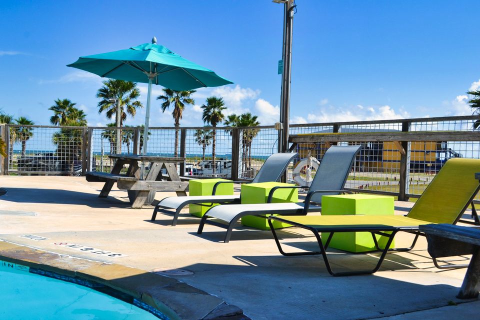 Loungers and a teal umbrella beside the pool, palms and the Gulf in the distance