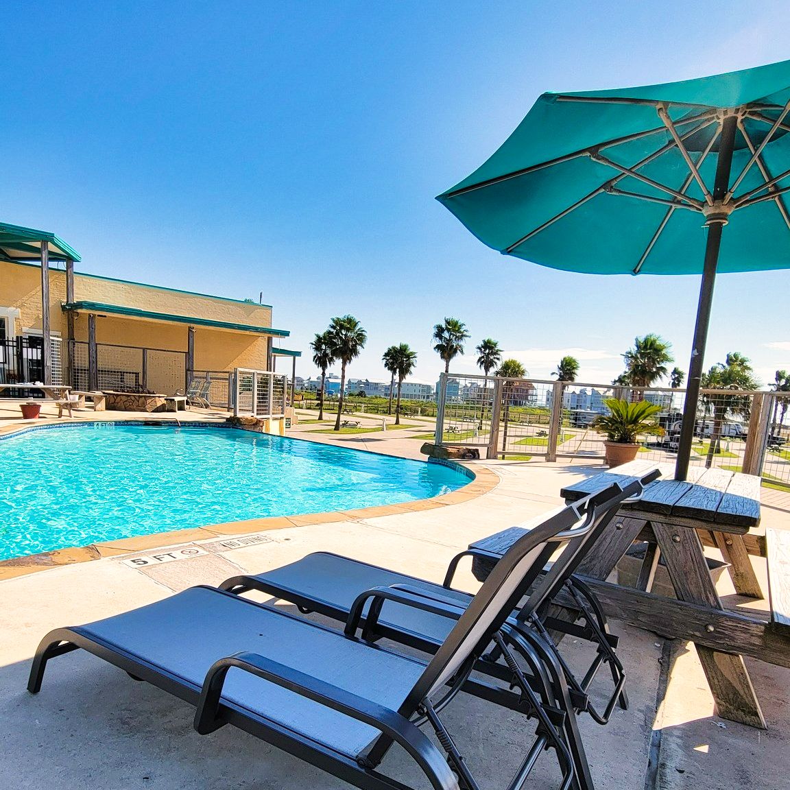 Pool deck with loungers and a teal umbrella at Sandpiper RV Resort