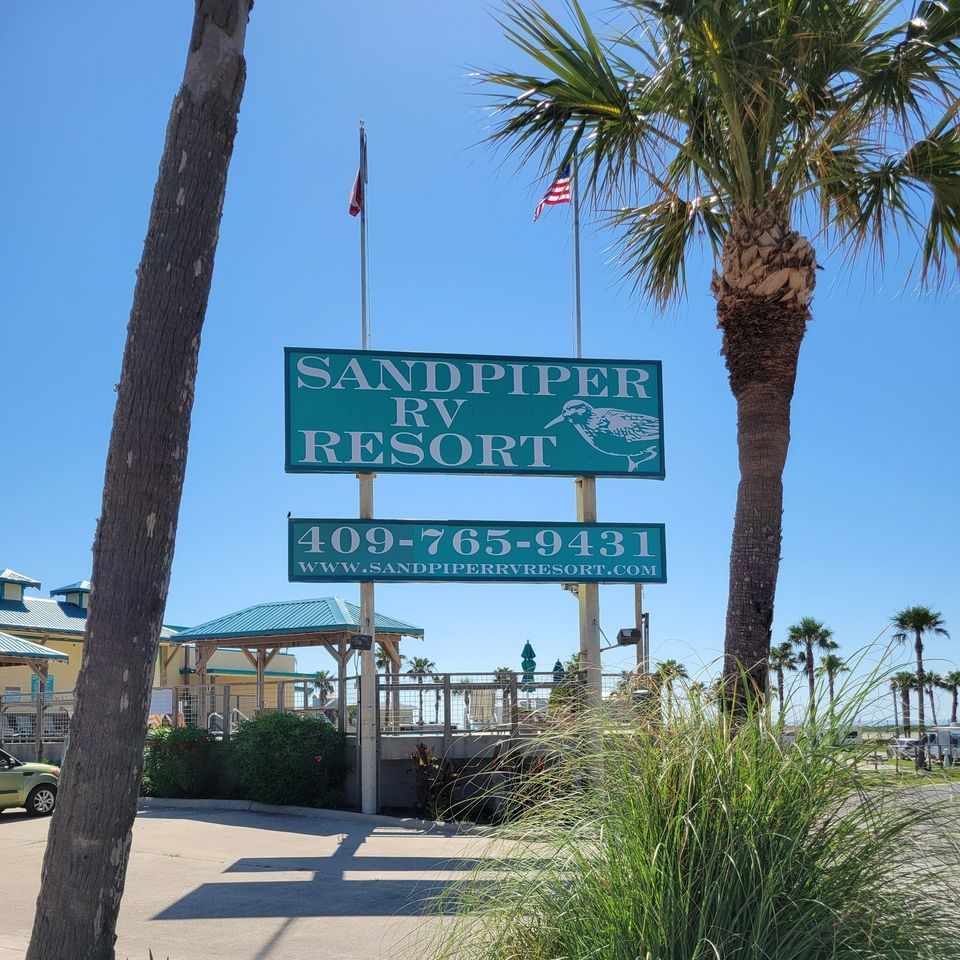 The Sandpiper RV Resort sign between palms with the Texas and United States flags