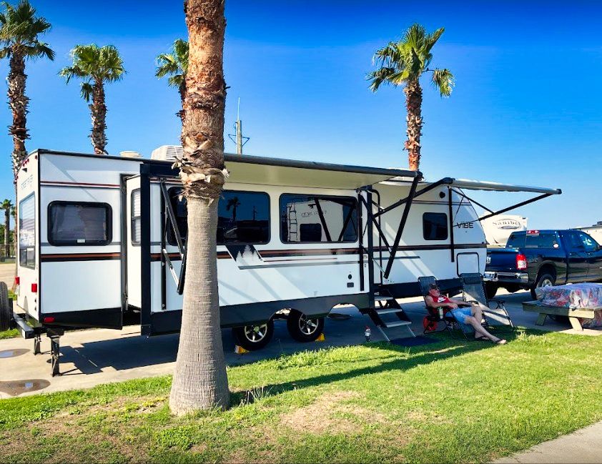 A travel trailer under palms on a concrete pad with a picnic table