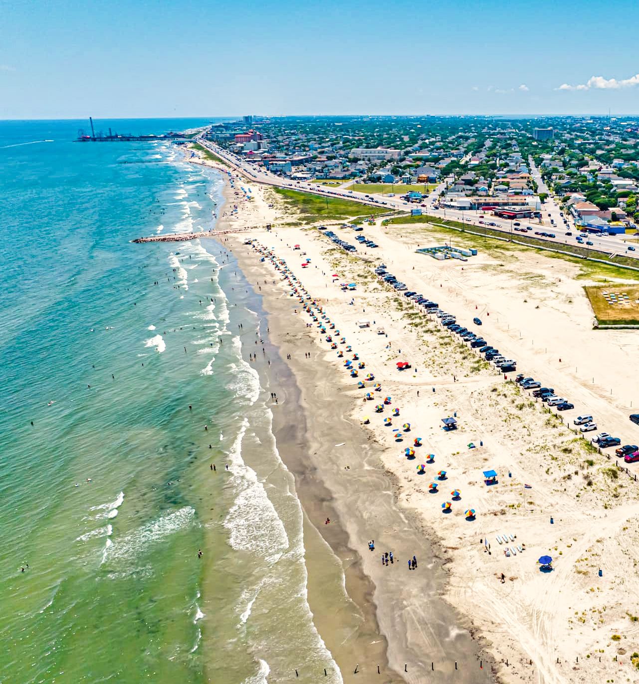Aerial view of Stewart Beach with umbrellas on the sand and the Pleasure Pier in the distance